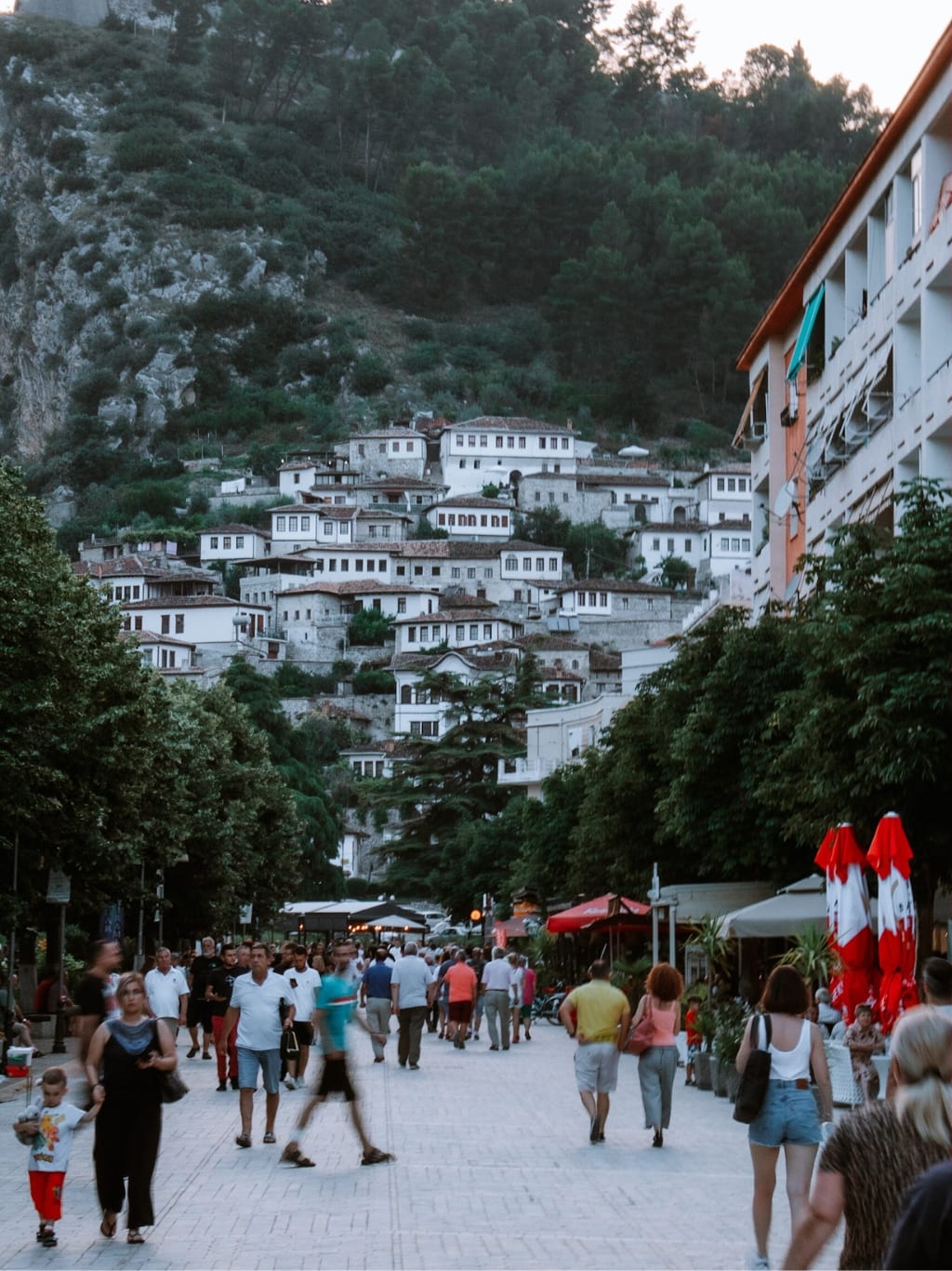 A photo of Bulevardi Republika in the evening, busy with families, friends, and couples walking down the street, overshadowed by the Ottoman buildings in the background, leading up the hill.