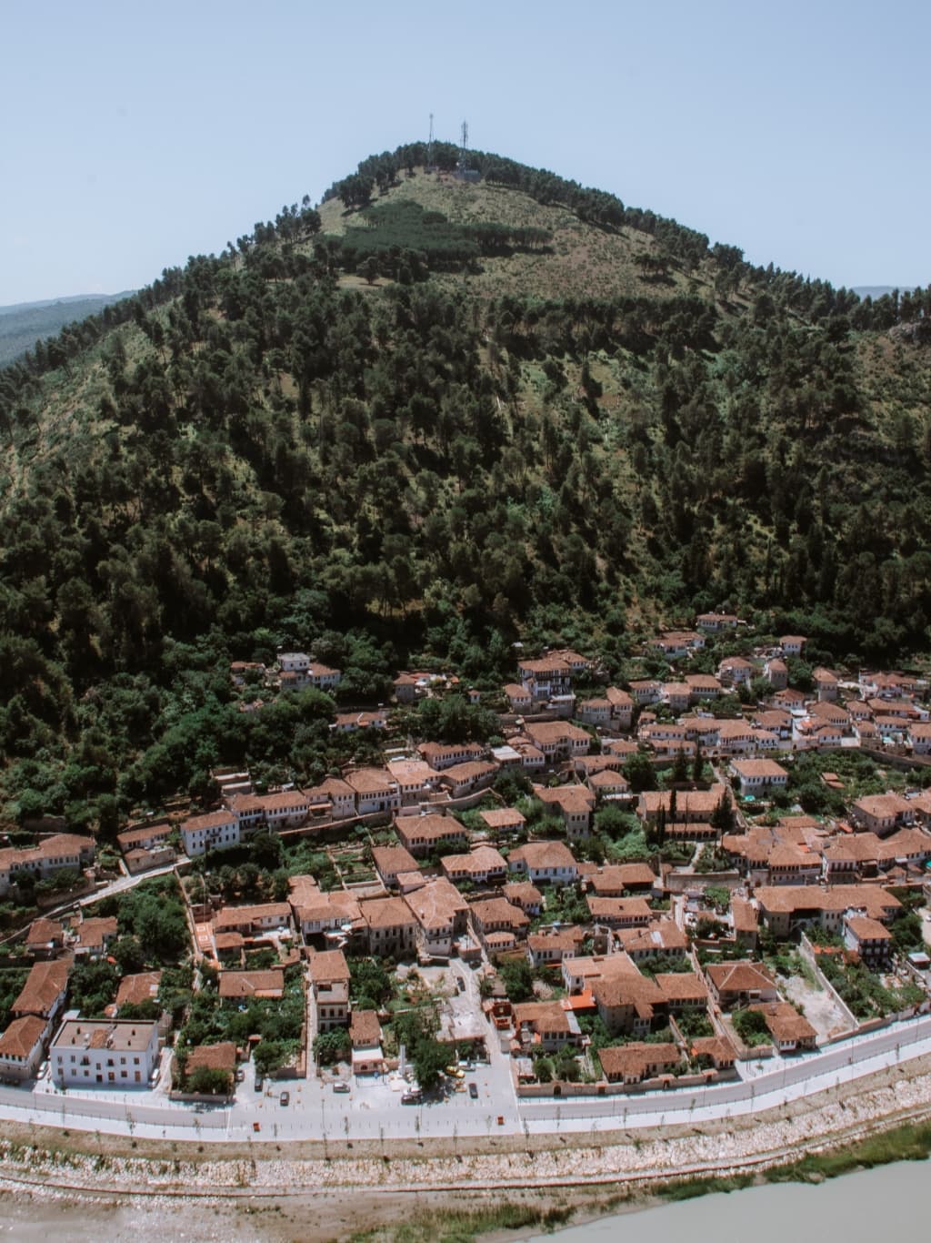 A photo from Berat Castle's viewing platform, showing the tall, green, pointed Gorica Hill, with the orange roofs of the Gorica District spread at the bottom of the hill