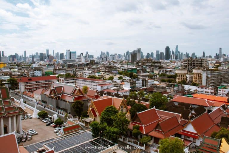 Bangkok cityscape captured from above, with a contrast of traditional red-roofed temples and modern skyscrapers under a bright sky, reflecting the city's evolving yet safe urban environment.